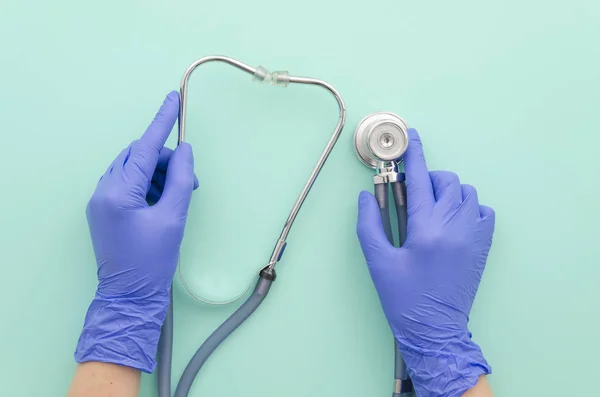 Läkare händerna i blå handskar med stetoskop på mint bakgrund. Medicinska begrepp. Ovanifrån. Lekmanna-platt. — Stockfoto