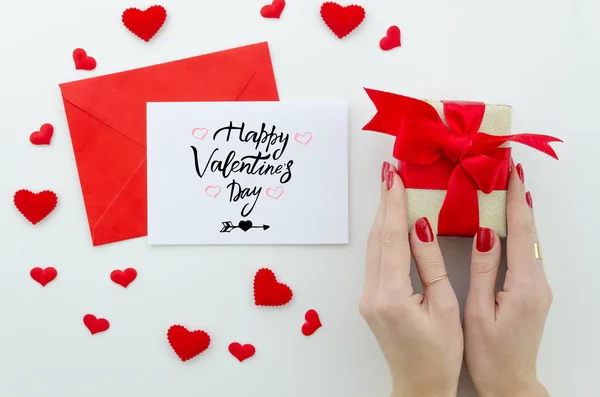 Valentine 14 february hand lettering greeting card. gentle composition for Valentines day woman hands holds gift box with red bow, many little red hearts top view. Flat lay