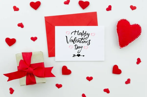 Kaart voor Valentijnsdag, rode speelgoed hart en een geschenkdoos met rode strik op een witte achtergrond. Bovenaanzicht hand belettering wenskaart — Stockfoto