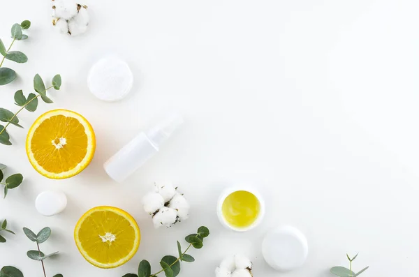 Flat lay home made cosmetics concept. Corner frame with green eucalyptus ,oranges, cotton flowers and cosmetic jars. Top view mockup. Minimal natural eco friendly design