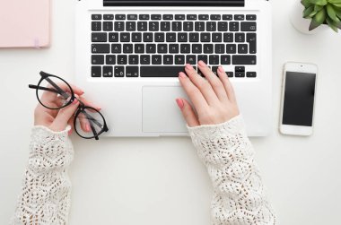Top womans görünümünü laptop tuş takımında yazarak eller ve beyaz Ofis Masaları boş smartphone, Not defteri ve dekoratif bitki üzerinde gözlük tutar. En az düz lay kadar alay