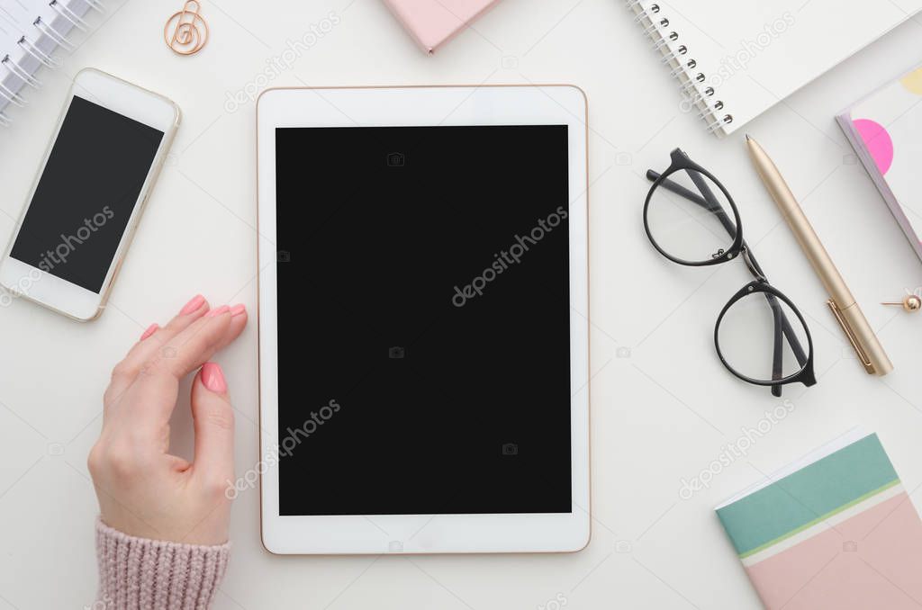 Mockup. Girl hand and digital tablet with blank screen, smartphone and notepad on table. Woman office workspace. Blog concept.
