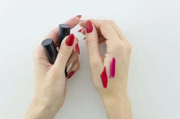 Probando el producto del maquillaje una muestra del lápiz labial rojo en la mano de la mujer con uñas rojas de la manucura hermosa.Vista superior . — Foto de Stock