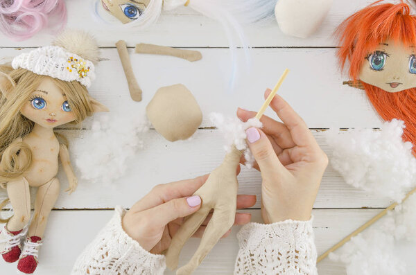 Woman in the process of creating handmade doll, top view, seamstress workplace, many object for needlework, embroidery, sewing supplies, handicraft, creation process, fancywork on a wooden background.