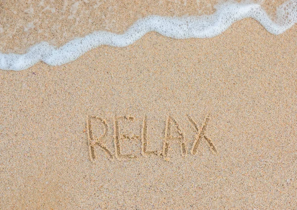 Palabra Relajarse escrito a mano en la playa de arena. Concepto de viaje. Vacaciones de verano — Foto de Stock