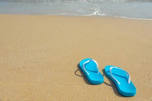 Concepto de vacaciones tropicales de verano. Chanclas en una playa de arena oceánica. Zapatos de playa azules en la orilla del mar de arena . — Foto de Stock