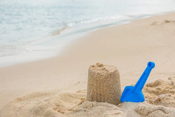 A sandcastle on the sand of a beach with blue shovel. Summer vacations. Happytime. Copy space for banner, flyer, poster. Seaside holidays concept