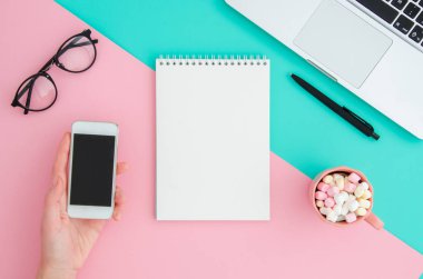 Üst görünüm dizüstü bilgisayar, gözlük ve pembe ve nane arka plan masaüstünde telefon tutarak boş not defteri yatık