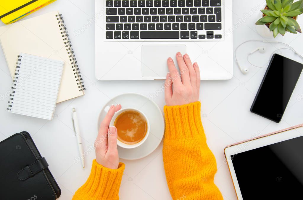 Top view of a woman blogger in a yellow knitted sweater working at notebook. Flat lay workplace white desktop