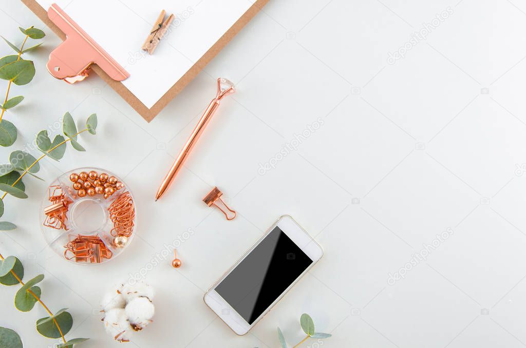 Flat lay beautiful Stylish workspace. Fashion women blogger workspace with a smartphone, cotton flowers, eucalyptus branches and rose gold office supplies top view background.
