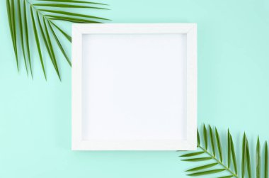 Daire, palmiye ağacından tropikal yaprakları ile açık mavi arka planda boş kağıt listesinde kopya alanı ile beyaz çerçeve yatıyordu. Üst görünüm mockup