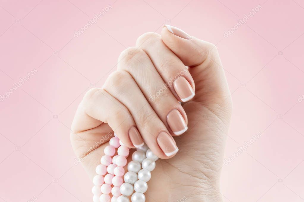 Beautiful french manicure nail studio. Natural nail art design. Woman hand with a pearl necklace.