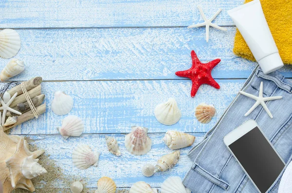 Summer sea beach concept. Top view blue wooden planks with seashells, rocks, sand and sunblock cream. White phone with blank screen and space for banner