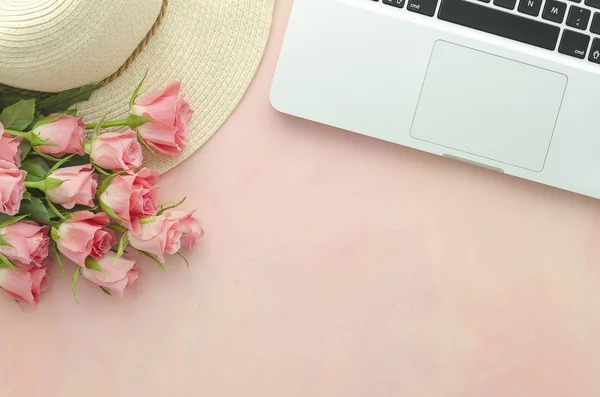 Womens workplace flat lay with pink roses on a pink background with a laptop and a straw hat. Copy space top view