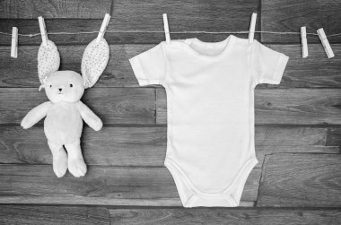 Ahşap bir arka plan üzerinde oyuncak tavşan ile bir çamaşır ipi üzerinde üst görünümü beyaz bebek bodysuit. Metin mockup için alan kopyalama