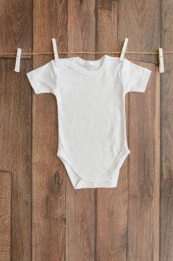 Dikey düz ahşap bir arka plan üzerinde klipler ile bir ip üzerinde asılı beyaz bebek bodysuit yatıyordu. Metin yazısı için boşluk kopyalama