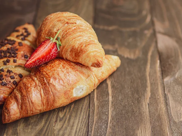 French breakfast. Closeup croissants with strawberry on a wooden planks background