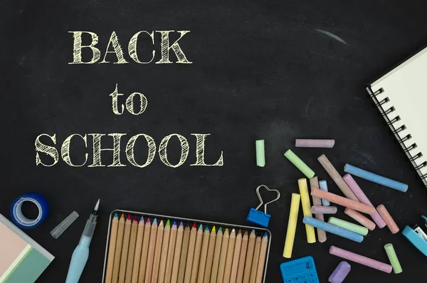 Flat lay tationery, notepads, pencils and clips over classroom blackboard with white chalk sign. Back to school concept