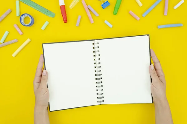 Flat lay mockup students hands holds blank notepad. Top view framed with tationery and chalks