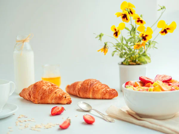 Desayuno de verano con un tazón de ensalada de frutas frescas saludables, croissants y leche. Mesa blanca con flores amarillas — Foto de Stock