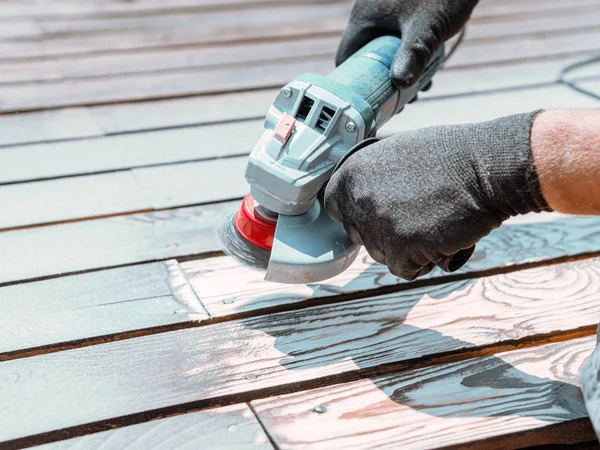 Male hands polishing dark wooden plank with angle grinder and metal brush