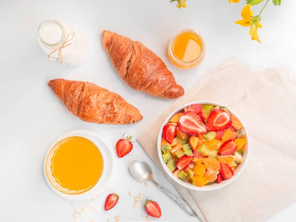 Flat lay desayuno de verano con tazón de ensalada de frutas frescas saludables, taza de té y croissants sobre fondo blanco — Foto de Stock