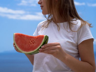 Beyazlı kadın deniz sahilinde bir dilim karpuz tutuyor. Renkli yaz konsepti
