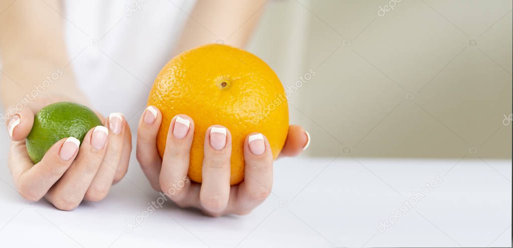 Female Hands with French Manicure on Nails Holding a Fresh Summer Orange and Limet Fruits. Horizontal banner with copy space for text
