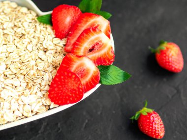 Çilek ile yulaf ezmesi yakın. Süt ile lapası. Diyet kahvaltısı. Siyah artalanları üzerinde kalp şekli seramik plaka