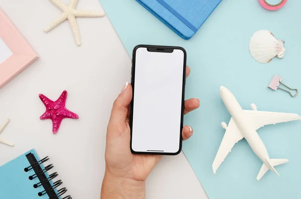 Man hand holding the black smartphone X with big blank screen and modern frame less design. Top view travel mockup with airplane and starfishes — Stock Photo, Image
