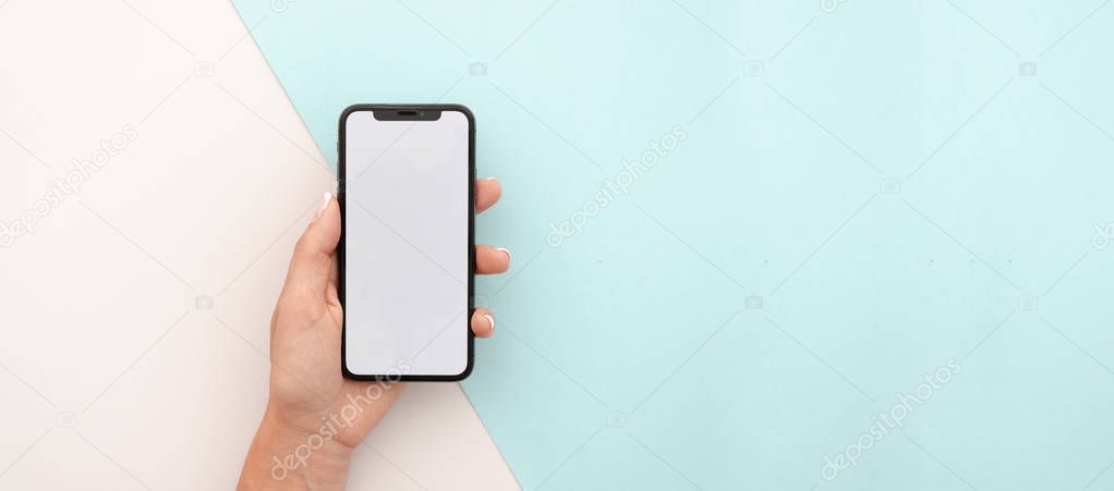 Man hand holding the black smartphone X with big blank screen and modern frame less design. Top view travel mockup horizontal banner