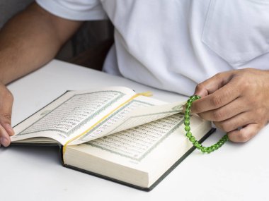 Adam Kur 'An kitap okuma ve Islam tespih tutar. İslam konsepti. Kuran Kareem kitap kapak Arapça harfler ile yazmak