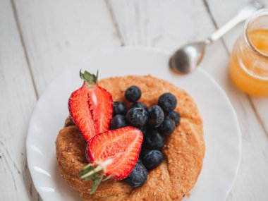Beyaz bir arka planda yaban mersini ve çilek ile taze simit. İngilizce yaz kahvaltısı. Yatay çekim