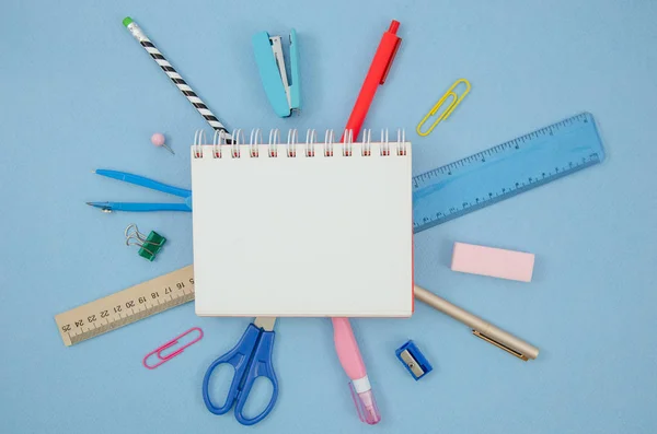 Concetto di scuola laica. Mockup dello spazio di lavoro con blocco note a spirale vuoto e spazio per copiare, pennarelli, graffette, forbici, righello. Cancelleria su un tavolo blu — Foto Stock