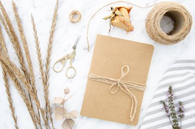 Üst görünüm sanat ve zanaat araçları seti, kraft kağıt kapaklı dizüstü bilgisayar. Mermer arka plan üzerinde lavanta, ip, okaliptüs ve buğday yaprakları