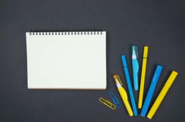 Düz okul konsepti, boş spiral defter ve kopyalama alanı, mavi ve sarı keçeli kalemler, ataçlar ile çerçeve geri mockup yatıyordu. Kara tahta arka planda kırtasiye