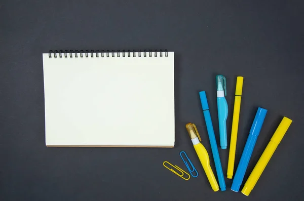 Plana maqueta de vuelta al concepto de la escuela, marco con cuaderno en espiral en blanco y espacio de copia, plumas de fieltro azul y amarillo, clips de papel. Papelería sobre un fondo de pizarra —  Fotos de Stock
