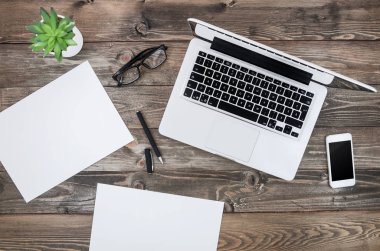 Düz bir gümüş dizüstü bilgisayar ve beyaz akıllı telefon ile mockup blogger işyeri ahşap masa yatıyordu. Vintage tonda kopya alanı olan boş kağıt listeleri