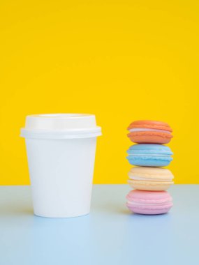 Renkli macaroons ile Mockup beyaz kağıt kahve fincanı. Sarı arka planda yan görünüm. Metin için Boşluk Kopyalama