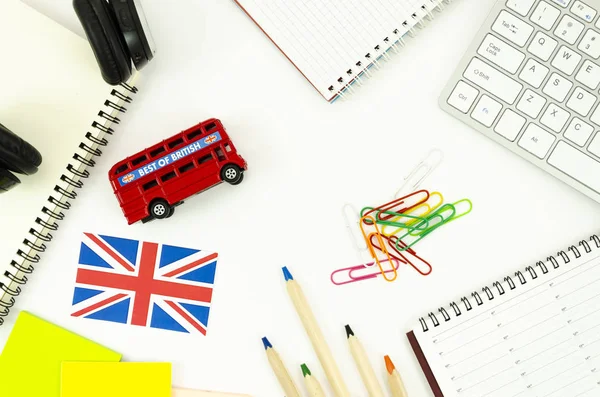 Flat lay frame student desktop with blank spiral notepads, earphones, British bus toy and Britsh flag. Top view language learning concept