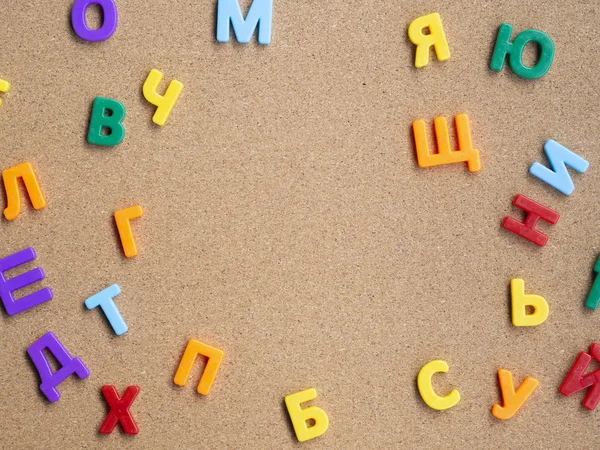 Marco de letras magnéticas plásticas cirílicas de colores en el escritorio de corcho. Aprender idiomas concepto —  Fotos de Stock