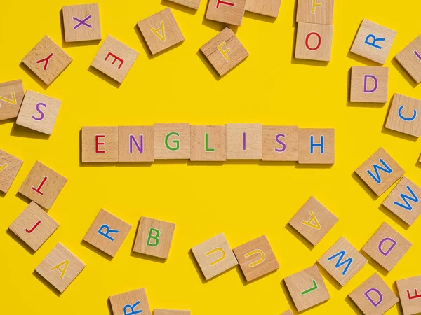 Концепция изучения языка высшего уровня. Слово "английский" из букв "habet" на деревянных кубиках на желтом фоне — стоковое фото