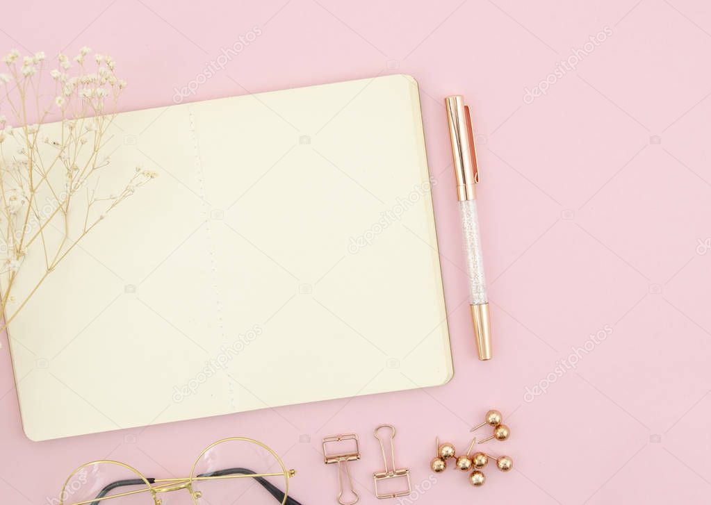 Female still life concept on pink background. Top view with rose gold stationary and pen, reading glasses and opened blank notepad. Flat lay mockup