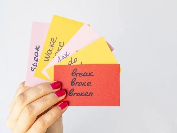 女性手拿卡片，手用手写的不规则英语动词在灰色上隔离。外语学习理念 — 图库照片