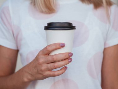 Hipster blond girl holding white coffee to go while, mock-up of coffee cup with copy space clipart