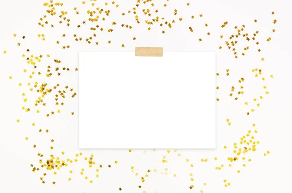 Вечірка запрошує макет сцени з золотистою зіркою, що блищить конфетті і закріплений порожній список паперу. Білий фон. Вид зверху — стокове фото