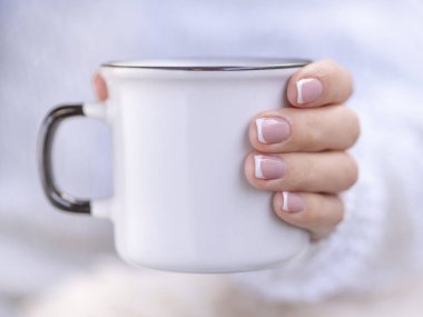 Samimi örülü kazaklı bir kadın elinde bir kış bardağını tutuyor. Fransız manikürlü zarif tırnakları olan, beyaz seramik bardakta fotokopi çeken kadın elleri. Kış ve Noel zamanı kavramı