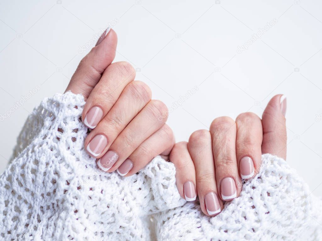 Female hands in cozy knitted sweater demonstrate fingernails with natural color nail polish and french manicure. Manicure and beauty treatment in winter time concept