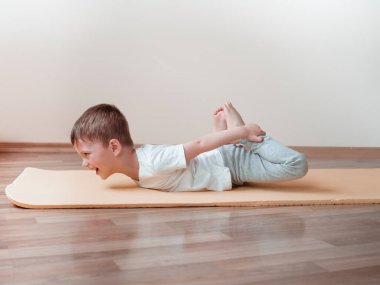 Yoga yapan küçük çocuk Dhanurasana, Bow Poose, evde. Çocuklar için evde spor