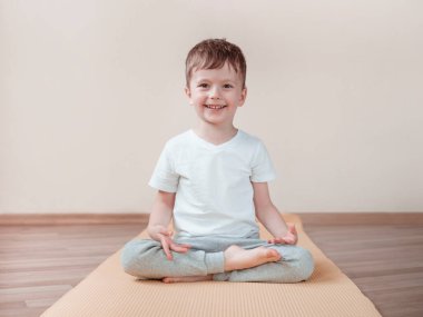 Çocuk yoga Lotusu pozisyonu ya da Padmasana üzerine meditasyon yapıyor. Ön manzara tam boy. Evdeki çocuklar için yoga egzersizleri.
